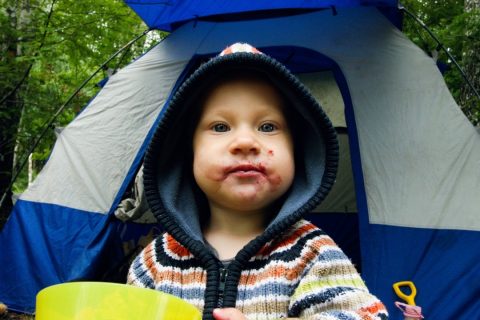 Infant camping grubby face in front of a tent