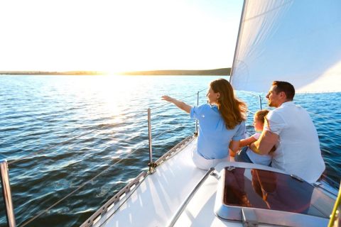 Parents and a child sitting on a boat pointing at something in the distance as they sail towards the sun