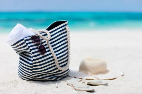 A large beach bag and sun hat sitting on the beach