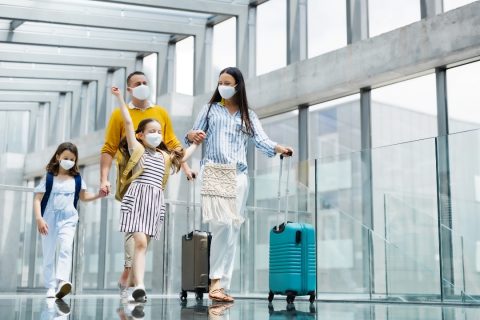Family in an airport with suitcases wearing face masks