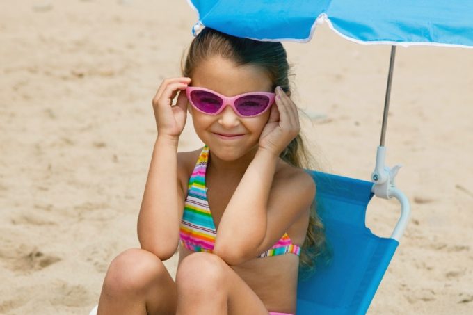 Girl with sunglasses sitting in ablue kids beach chair