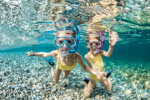 two girls swimming underwater in the ocean waving at a camera