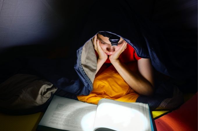 Boy reading a book by flashlight in a tent - guide to best kids camping flashlights