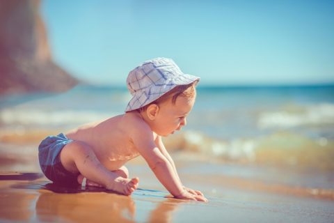 Cute baby crawling along a beach in a sun hat - essentials for bringing baby to the beach