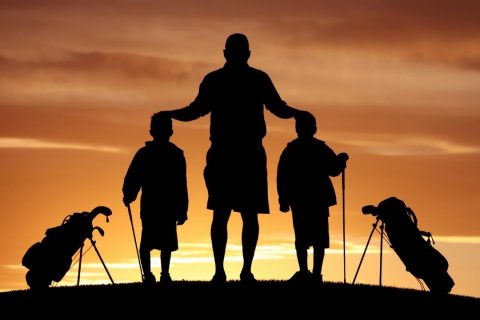 a father and two sons standing in silhoutee with their golf clubs and golf bags - family golf vacations