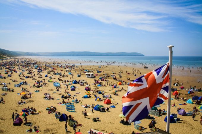 UK Flag flying over a busy English beach in summer - summer staycation ideas