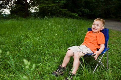 Young boy in a bright orange tshirt sitting in a blue kids camping chair - the best camping chairs for kids