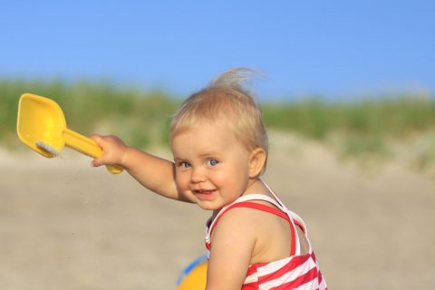 Baby on a beach playing with sand toys