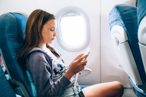 Tween girl sitting on an airplane playing with phone