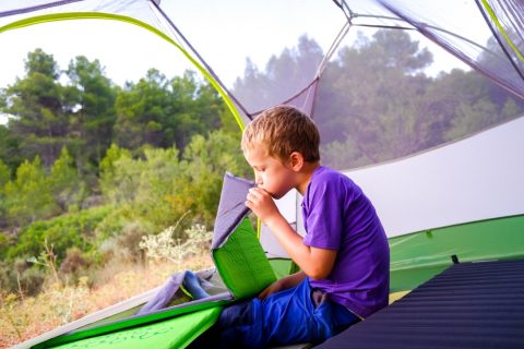 A child sitting in a tent blowing up a camping mat
