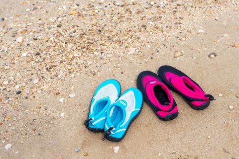 2 pairs of blue and pink water shoes for kids on a beach