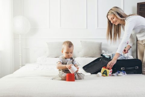 baby playing on bed while mother is packing a suitcase
