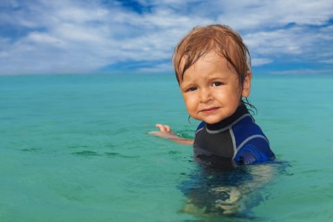 Toddler swimming in the ocean with a wetsuit