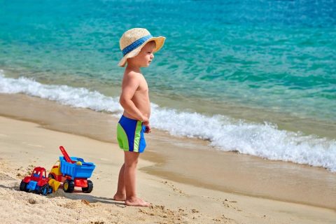 toddler boy standing on the beach with his beach toys