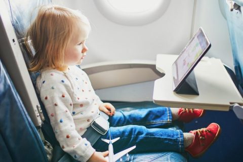 A toddler sitting on an airplane with a tablet in front of them